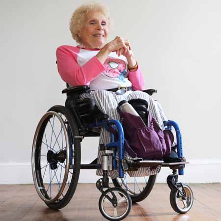 Woman with blond hair and pink sweater in manual wheelchair.
