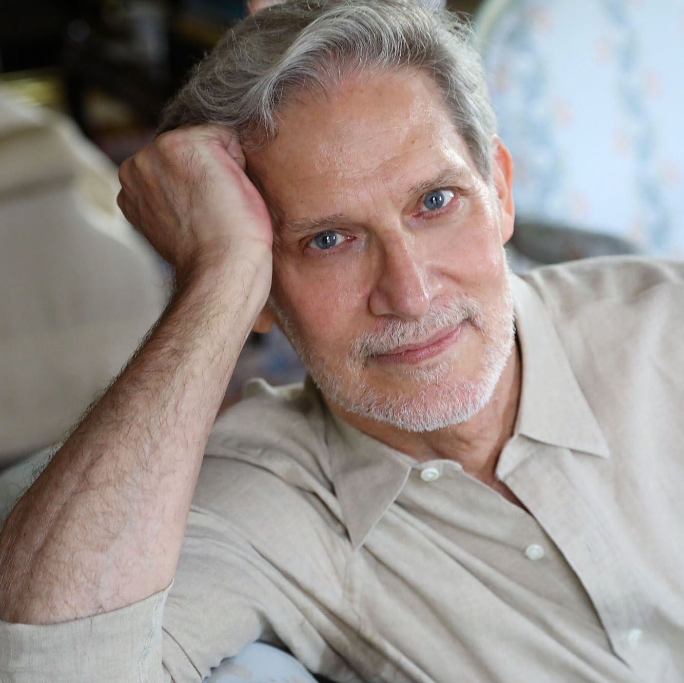 Man with grey hair and light beard in Tamn dress shirt, leaning on right hand and looking into the camera