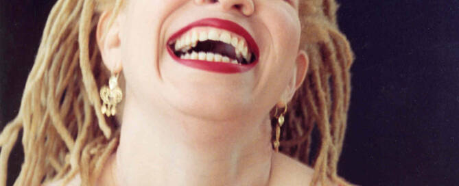 Woman with blond dreads and bright red lips laughing.