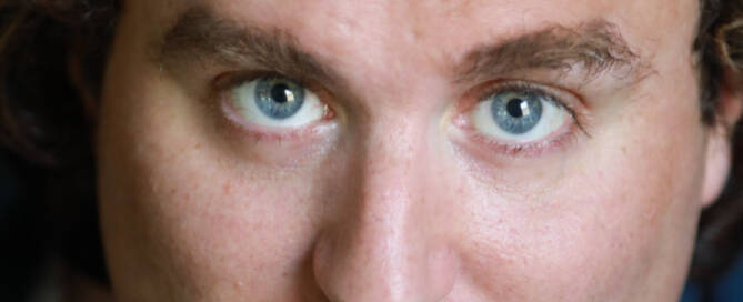 man with blue eyes and curly brown hair looking into the lens.