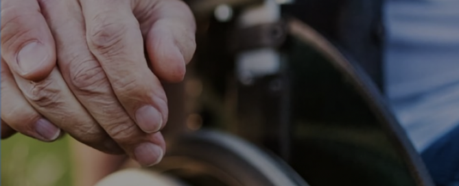 image of 2 hands holding each other, wheelchair section in background.