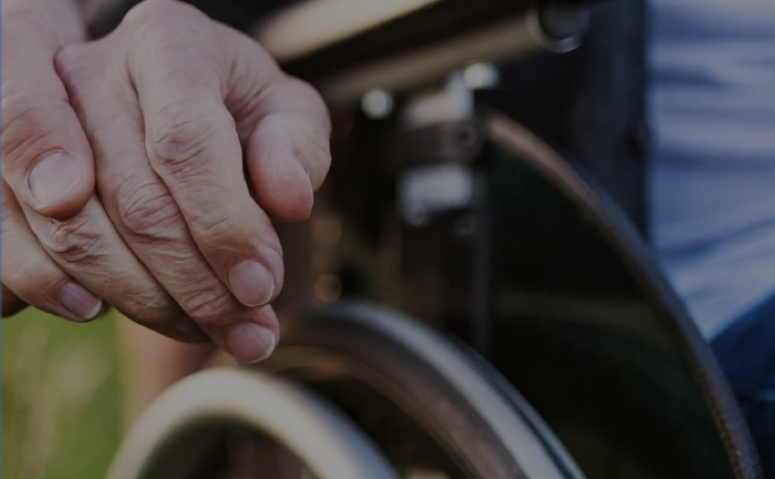 image of 2 hands holding each other, wheelchair section in background.