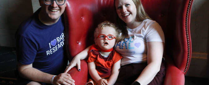 young boy with red glasses sitting on a red chair with his parents