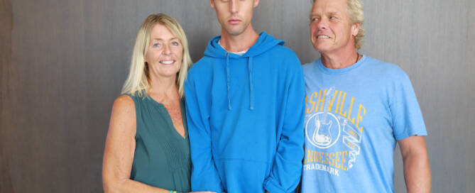 young man with Phelan-McDermid Syndrome wearing blue shirt standing next to his mother and father