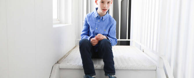 young boy with chromosome 5p- (Cri Du Chat) wearing blue shirt sitting on white steps