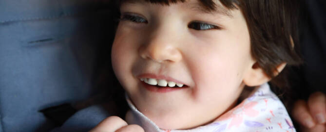 young girl with Phelan-McDermid Syndrome smiling and looking to the left, closeup photo.