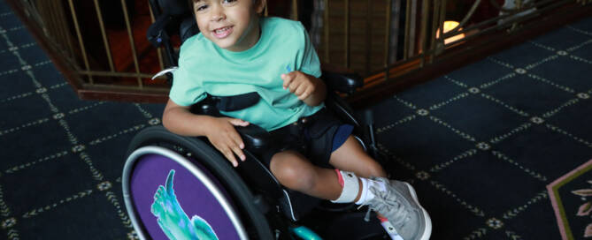 young boy with turquoise shirt in a wheelchair looking into the camera