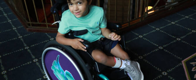 young boy with turquoise shirt in a wheelchair looking into the camera