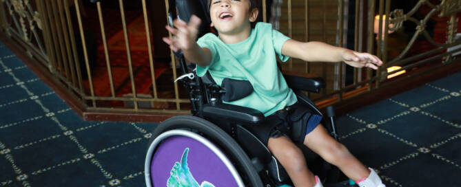 young boy with turquoise shirt in a wheelchair looking into the camera