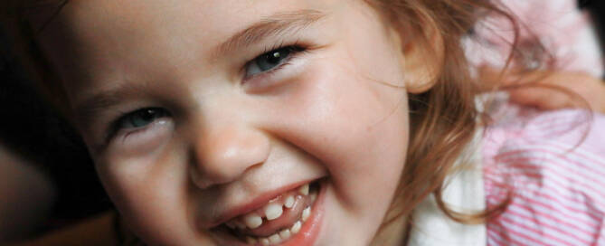 young girl wearing pink shirt smiling into the camera, closeup