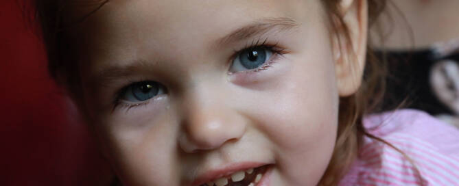 young girl wearing pink shirt smiling into the camera, closeup