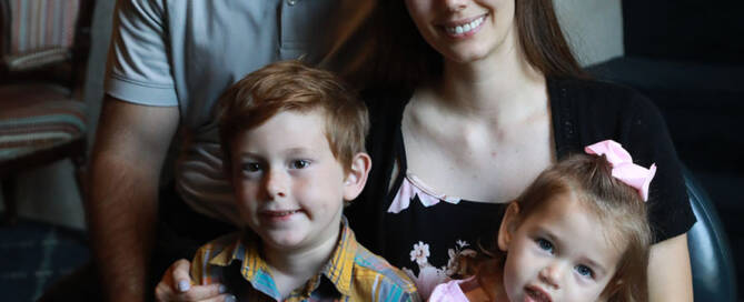 young girl with pink shirt poses with her mother, father, and brother