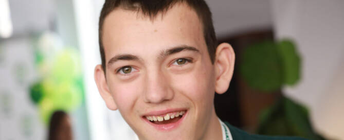 boy with Phelan-McDermid Syndrome wearing green shirt smiling at the camera