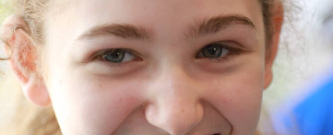 girl with Phelan-McDermid Syndrome wearing light blue headband smiling at the camera