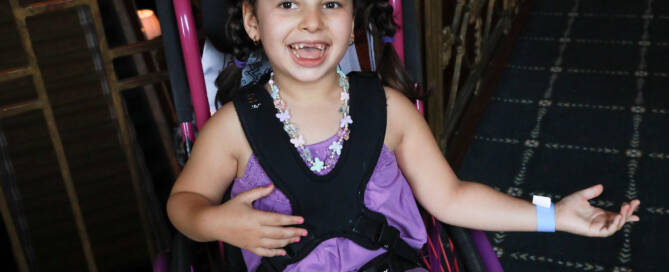 young girl wearing purple outfit in a wheelchair and smiling