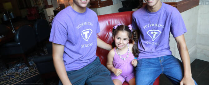 young girl in a purple shirt sitting in a red chair with her two brothers next to her