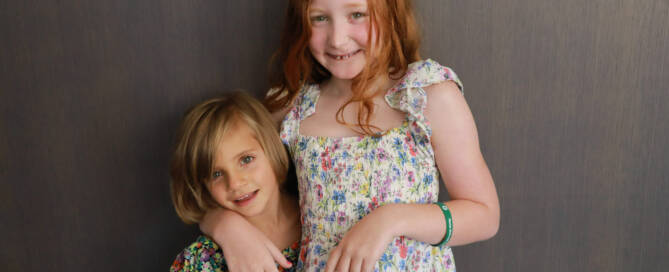 girl with Phelan-McDermid Syndrome wearing floral dress stands with another girl wearing a similar dress