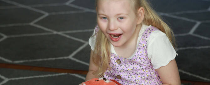 young girl with chromosome 5p- (Cri Du Chat) sitting on the floor and playing with a stuffed animal