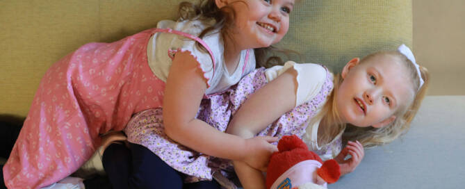 young girl with chromosome 5p- (Cri Du Chat) wearing pink dress plays on a couch with her sister