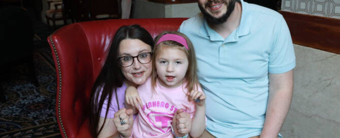 young girl wearing pink shirt and pink headband posing next to her mother and father