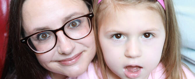 young girl with pink shirt and pink headband posing side by side with here mother, closeup photo