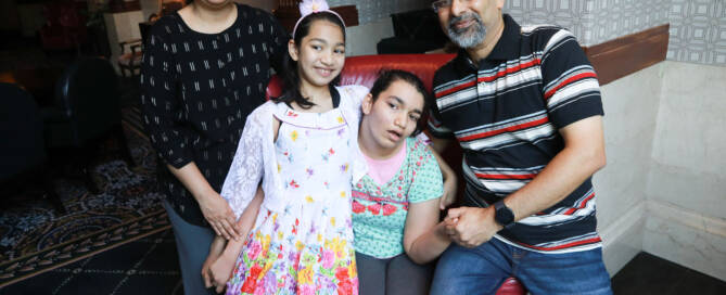 girl wearing green and red shirt sitting on red chair with her mother father and sister