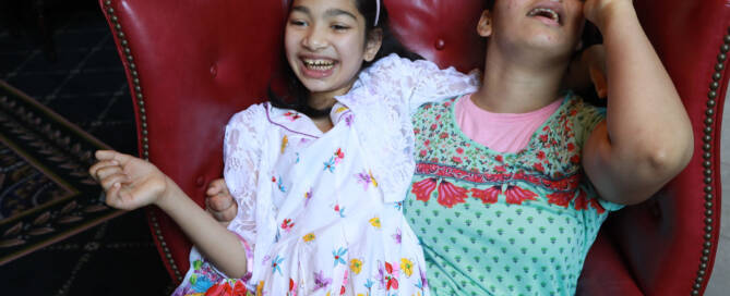 girl wearing green and red shirt sitting on a red chair with her sister