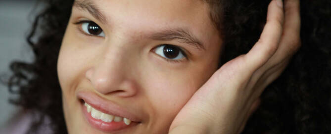 girl with chromosome 5p- (Cri Du Chat) rests her head on her hand and smiles at the camera