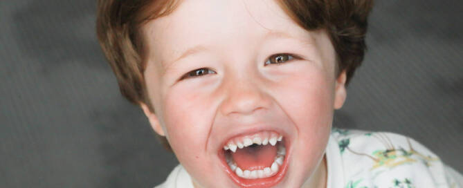 young boy with Phelan-McDermid Syndrome wearing white shirt gives a very excited look at the camera