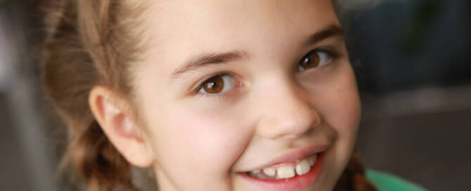 young girl with Phelan-McDermid Syndrome wearing green shirt smiling into the camera