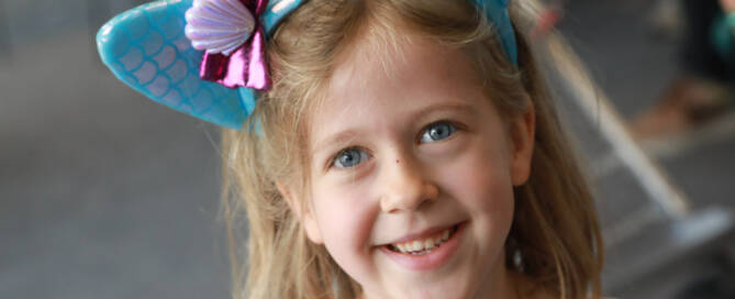 young girl with Phelan-McDermid Syndrome wearing blue cat ear headband smiling into the camera