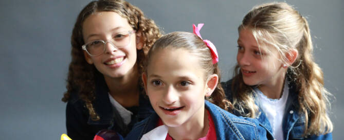 young girl with Angelman Syndrome surrounded by two other girls, all smiling