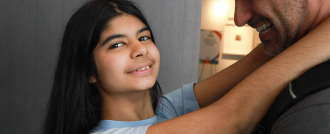 girl with Phelan-McDermid Syndrome wearing a blue shirt hugging her father and smiling into the camera