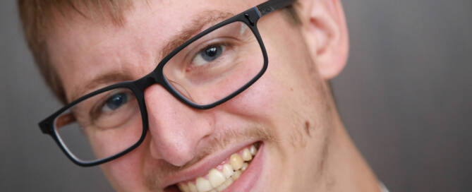 young man with Phelan-McDermid Syndrome wearing black glasses and smiling into the camera