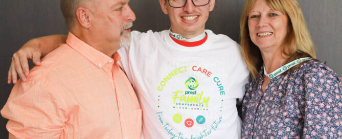 young man with Phelan-McDermid Syndrome wearing white shirt and black glasses posing with his mother and father for a photograph