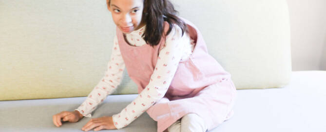 girl with chromosome 5p- (Cri Du Chat) wearing pink and white outfit sitting on couch while looking to the right