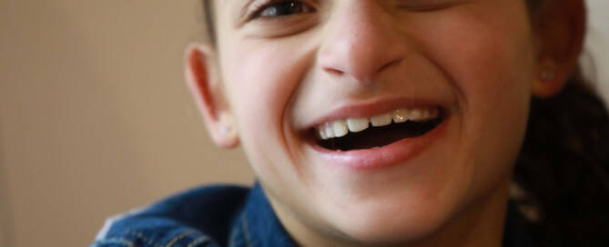 young girl with Angelman Syndrome smiling wide into the camera, closeup photo