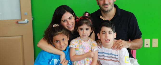 young boy wearing white shirt poses with his two sisters and mother and father