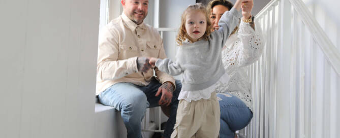 young girl with chromosome 5p- (Cri Du Chat) wearing grey shirt walks towards the camera while her parents hold her up