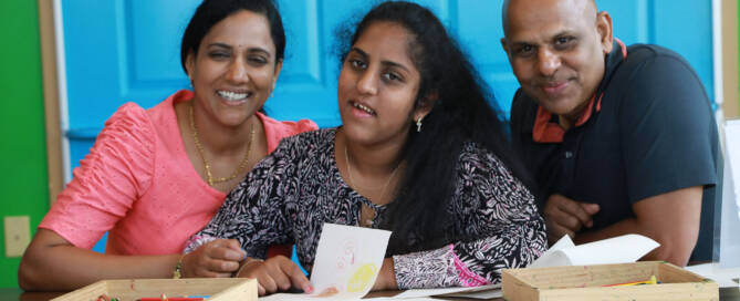 young woman poses with both her parents, blue background