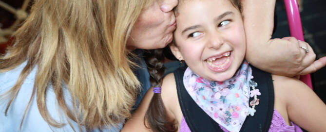 young girl wearing purple shirt gets kissed by her mother