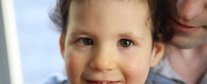 young girl with chromosome 5p- (Cri Du Chat) wearing grey shirt and pink boy smiling, closeup photo