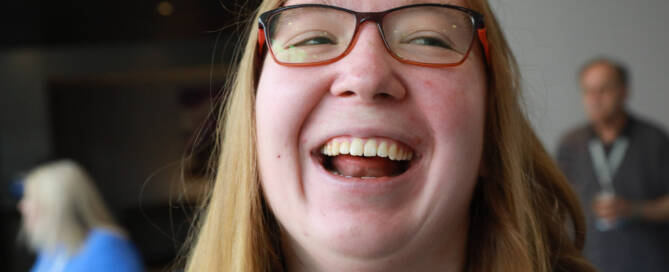 girl with Phelan-McDermid Syndrome wearing red and black glasses smiling wide while looking to the right