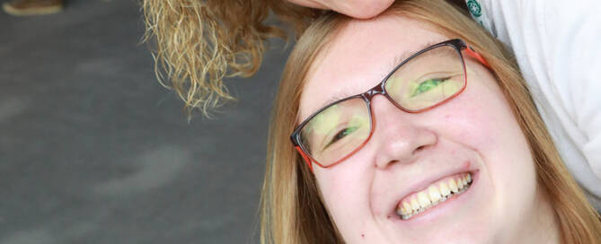 girl with Phelan-McDermid Syndrome wearing black and red glasses being hugged by her mother