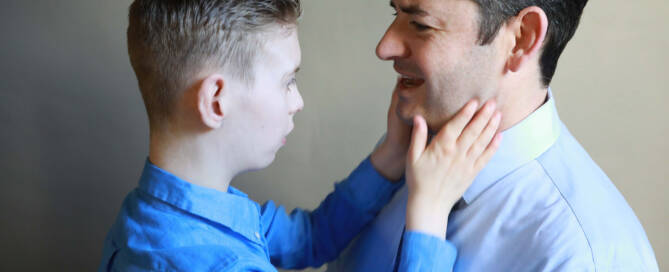 young boy with chromosome 5p- (Cri Du Chat) wearing blue shirt looking at his father touching his face