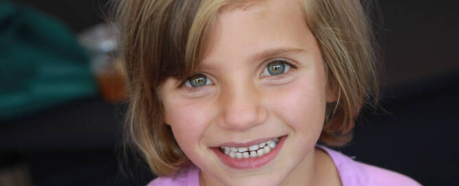 young girl with Phelan-McDermid Syndrome wearing pink shirt smiling at the camera, closeup photo