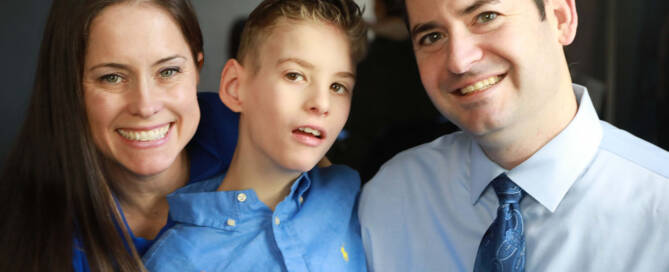 young boy with chromosome 5p- (Cri Du Chat) wearing blue shirt poses next to his mother and father