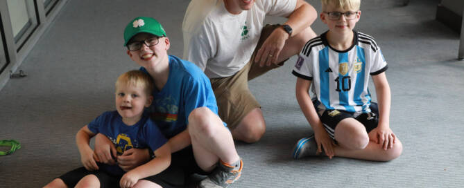 boy with Phelan-McDermid Syndrome sits on the floor with his father and two brothers