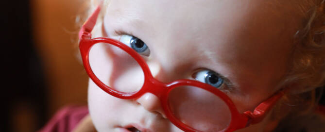 young girl with red glasses looks into the camera, closeup photo