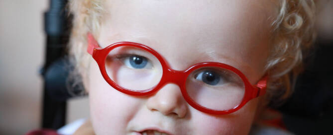 young girl with red glasses looks into the camera, closeup photo